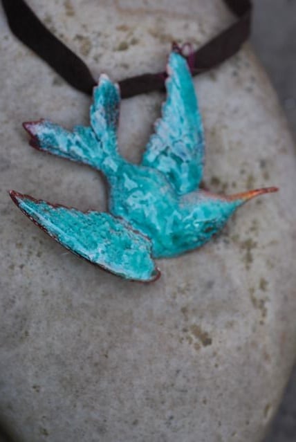 A turquoise ceramic bird figurine on a stone surface.