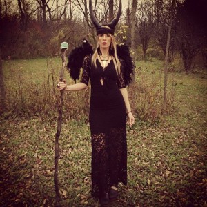 Woman in black costume with horns outdoors.