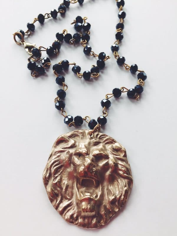 Gold lion head pendant with black bead necklace on white background.
