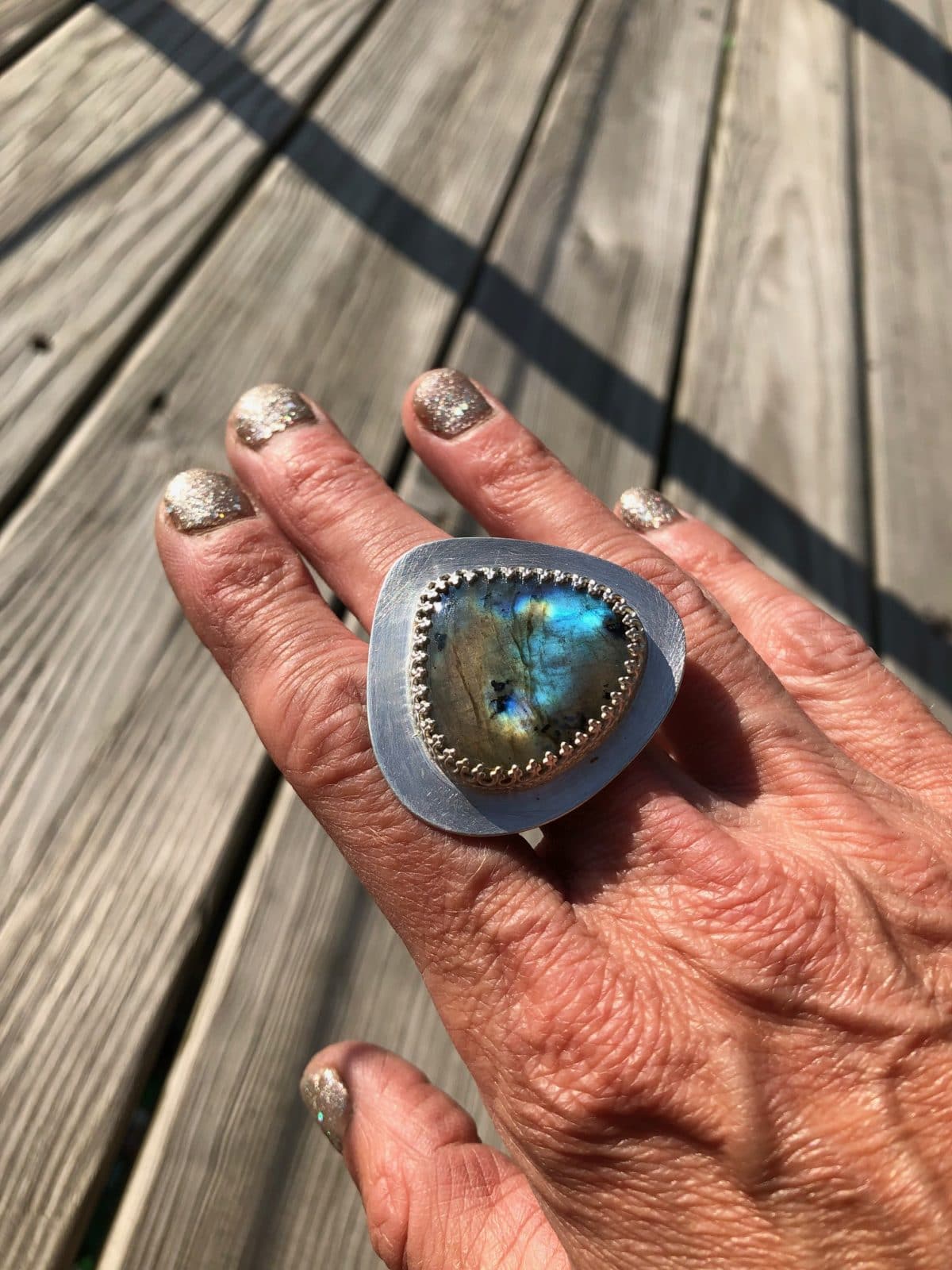 Hand wearing a large silver ring with a blue-green stone, nails painted glittery gold.