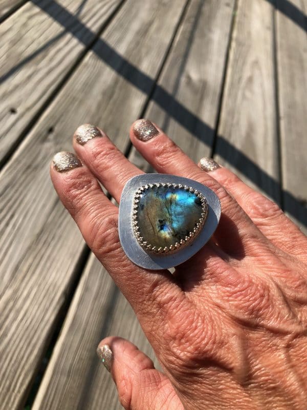 Hand wearing a large silver ring with a blue-green stone, nails painted glittery gold.