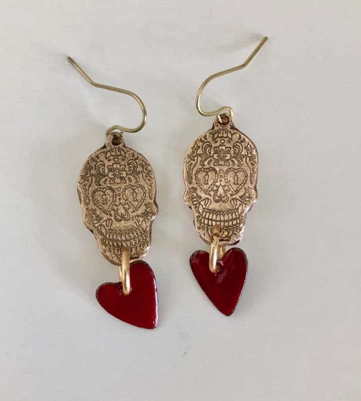 Gold skull earrings with red heart charms hanging below them.