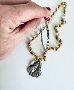 Hand holding a beaded necklace with a wolf pendant.