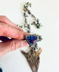 Hand holding a detailed necklace with a blue triangular pendant and an animal head charm.