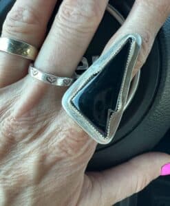 Hand with two rings, one silver with hearts and one large triangular black stone ring.