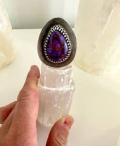 Hand holding a crystal with a decorative purple stone on top.