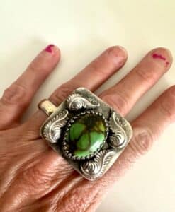 Hand wearing a large silver ring with a green stone and decorative engravings.