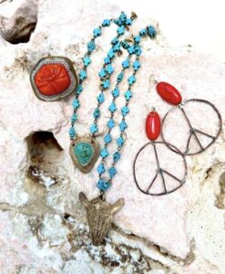 Turquoise cross necklace, red stone ring, and peace sign earrings on rock.