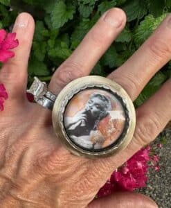 Hand wearing a large ring with a black and white portrait inside.