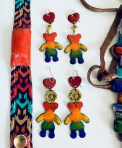 Colorful teddy bear earrings with hearts and flowers, alongside patterned fabric and beads.