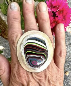 Hand wearing a large, colorful resin ring with layered patterns.