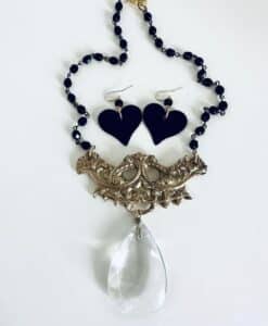 Black bead necklace with intricate gold centerpiece and large crystal pendant, paired with black heart earrings.