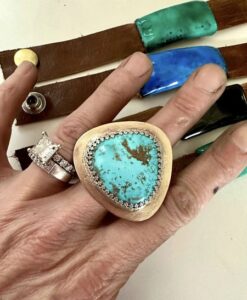 Hand with a large turquoise stone ring and diamond engagement ring.