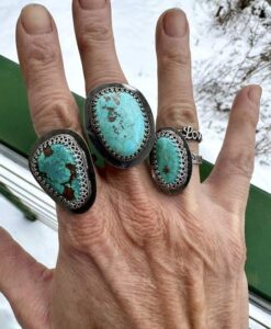 Hand adorned with three large turquoise rings and a silver 'Love' ring.