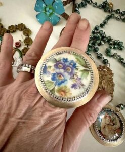 Hand wearing a large decorative ring with floral design and surrounded by jewelry.