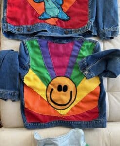 Colorful denim jacket with a large rainbow smiley face design on the back.