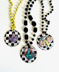 Three artistic pendants with hand and flower designs on checkered backgrounds.