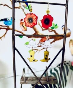 Earrings shaped like red flowers and yellow cowboy boots hanging on a display stand.