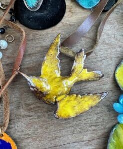 Yellow bird-shaped pendant with a leather strap on wooden surface.