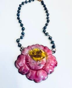 A necklace with a pink and yellow flower pendant on a black bead chain.