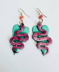 Colorful earrings with pink snakes coiled on green hearts and small pink flower hooks.