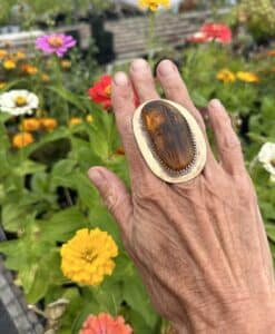 Hand wearing a large, rustic ring with a garden of colorful flowers in the background.
