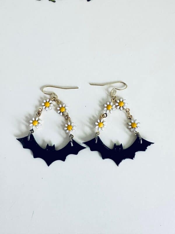 Earrings featuring black bats and small white daisies with yellow centers.