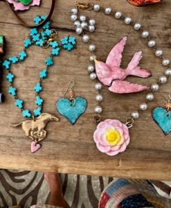Handmade jewelry including necklaces and earrings with hearts and bird designs on a wooden surface.