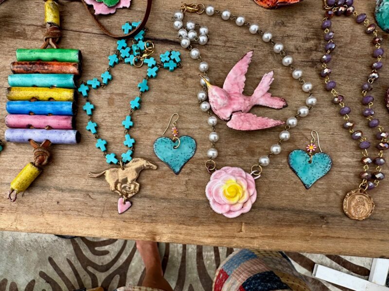 Handmade jewelry including necklaces and earrings with hearts and bird designs on a wooden surface.