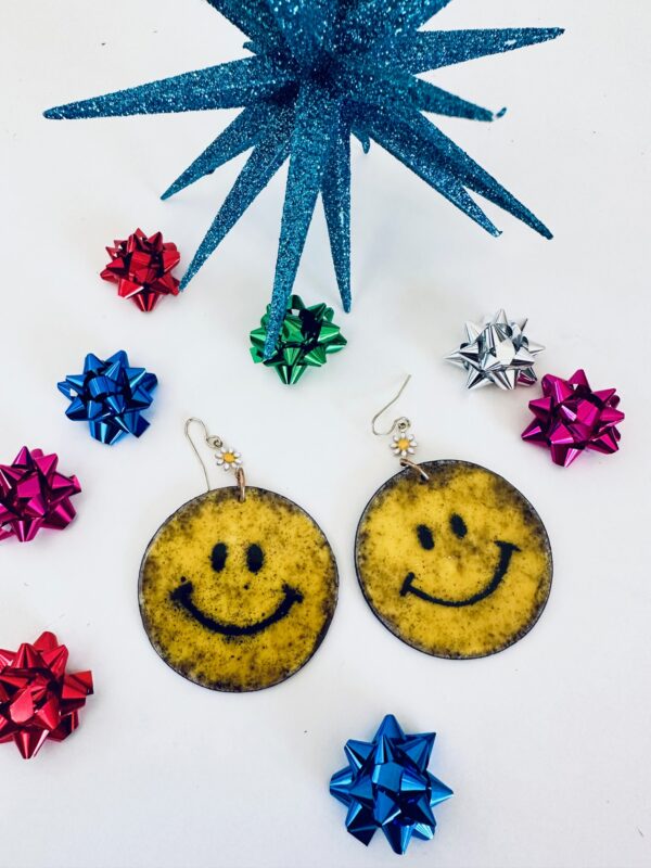 Smiley face earrings surrounded by colorful gift bows and blue star decoration.